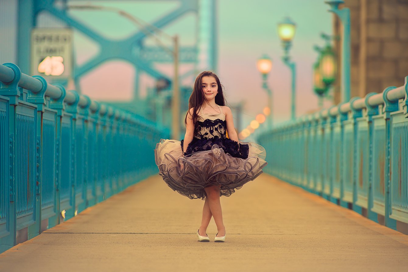 A fine-art child portrait on a blue Philadelphia bridge, blending editorial styling with a calm, thoughtful expression and soft city tones.