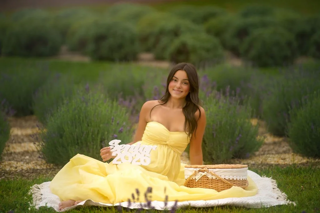 High school senior girl sitting in a lavender field holding a Senior 2026 sign during a South Jersey portrait session.