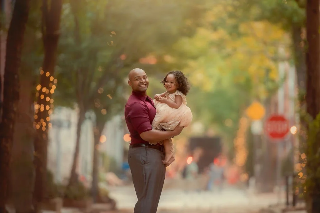 Father holding his daughter in the air as they smile together during a family session on Addison Street in Philadelphia.