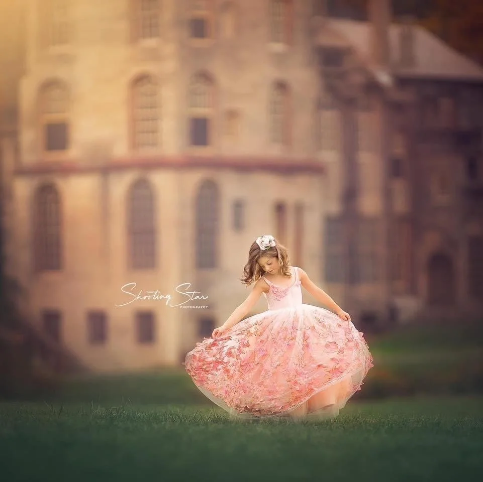 Girl wearing a pink dress twirling in front of a castle during a princess portrait session, captured in a fairytale setting
