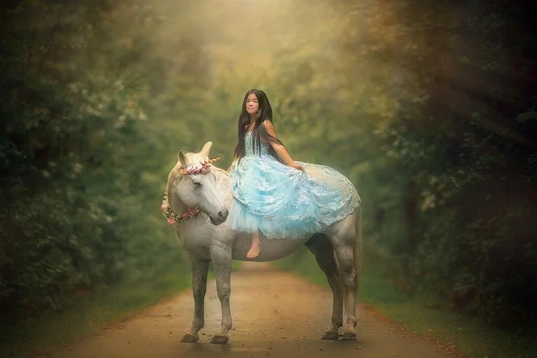 A fine art unicorn portrait featuring a child in a flowing blue gown seated calmly on a real unicorn photographed as part of a peaceful, child-led unicorn storybook for families across New Jersey, New York and Pennsylvania