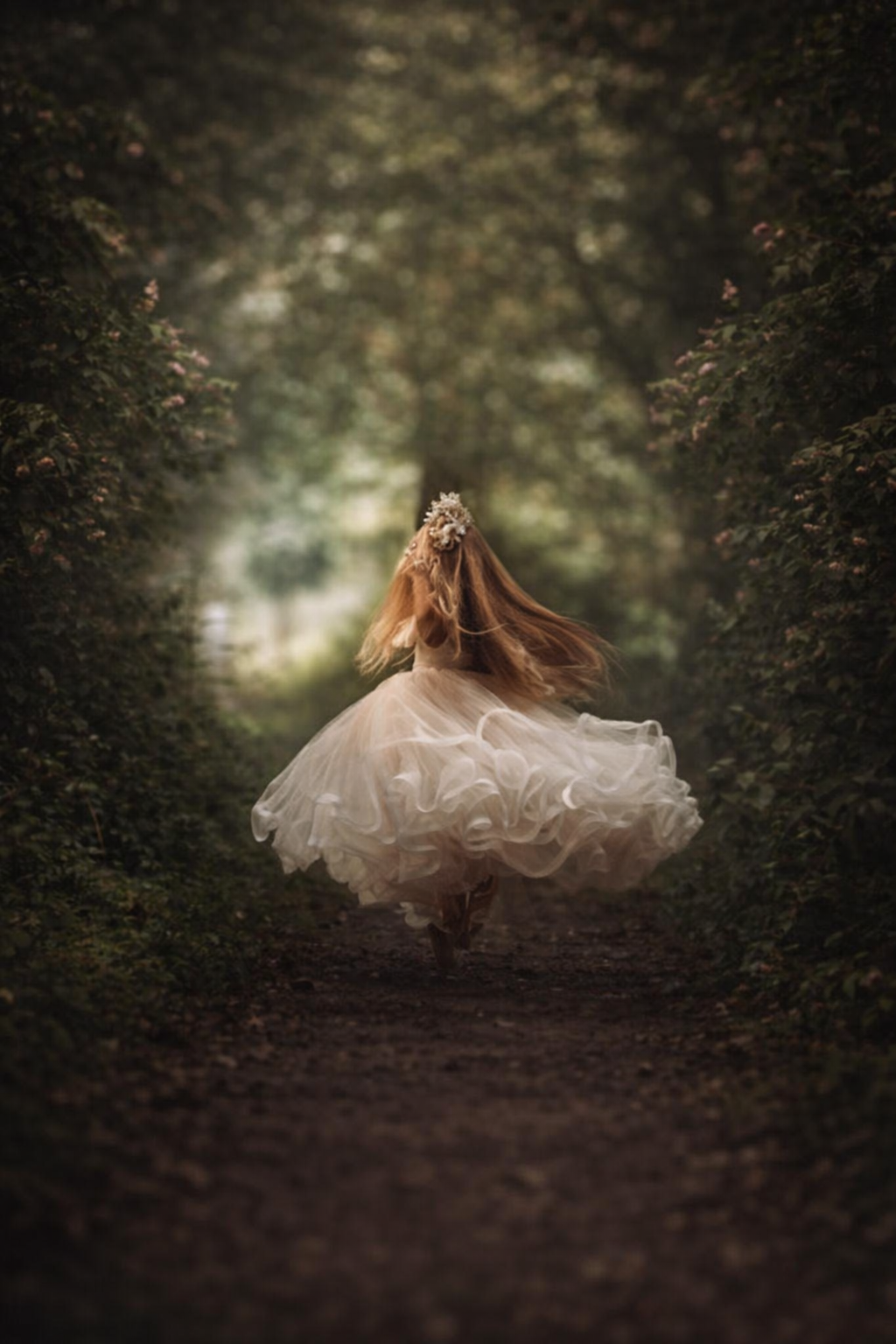 Little girl twirling in a flowing dress during an outdoor fine art mini session in a wooded garden setting