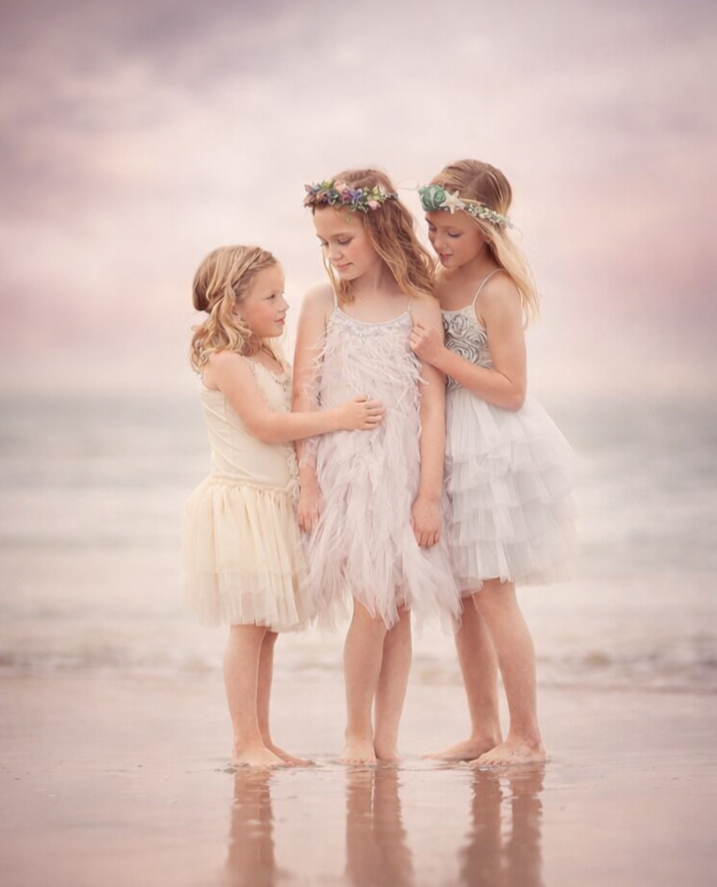 two sisters in pastel dresses holding hands during a Jersey Shore portrait session at sunset on the beach