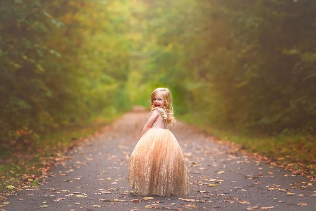 Young girl smiling over her shoulder during a family maternity photography session outdoors in South Jersey.