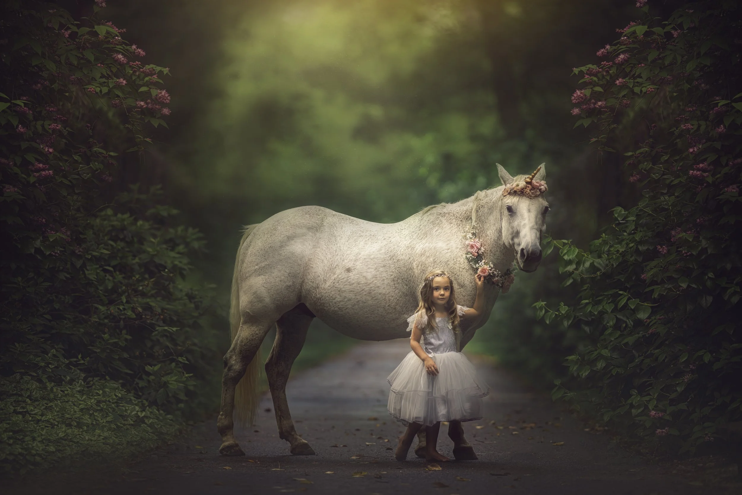 Little girl in a silver dress posing in a forest during a magical unicorn portrait session in South Jersey.