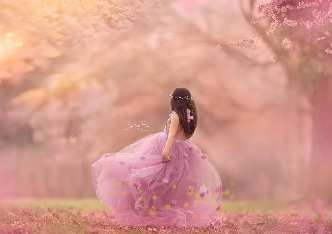Back view of a young girl twirling beneath cherry blossoms during a spring portrait session in Cherry Hill, New Jersey.