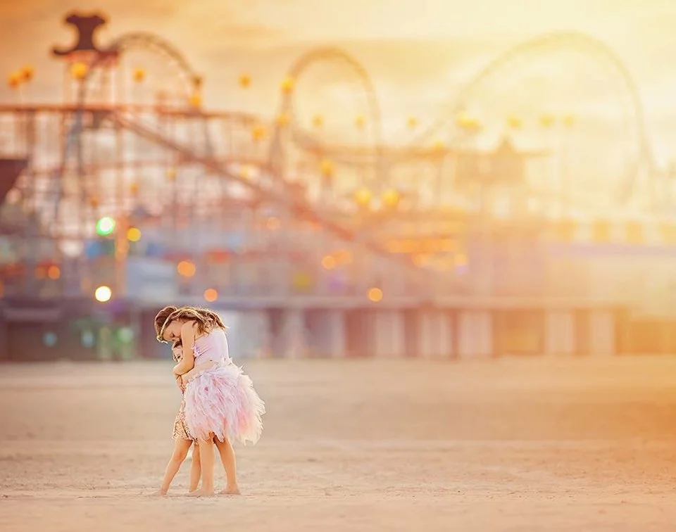 Two sisters hugging during a fine art beach photo shoot near the rollercoaster in Wildwood, New Jersey