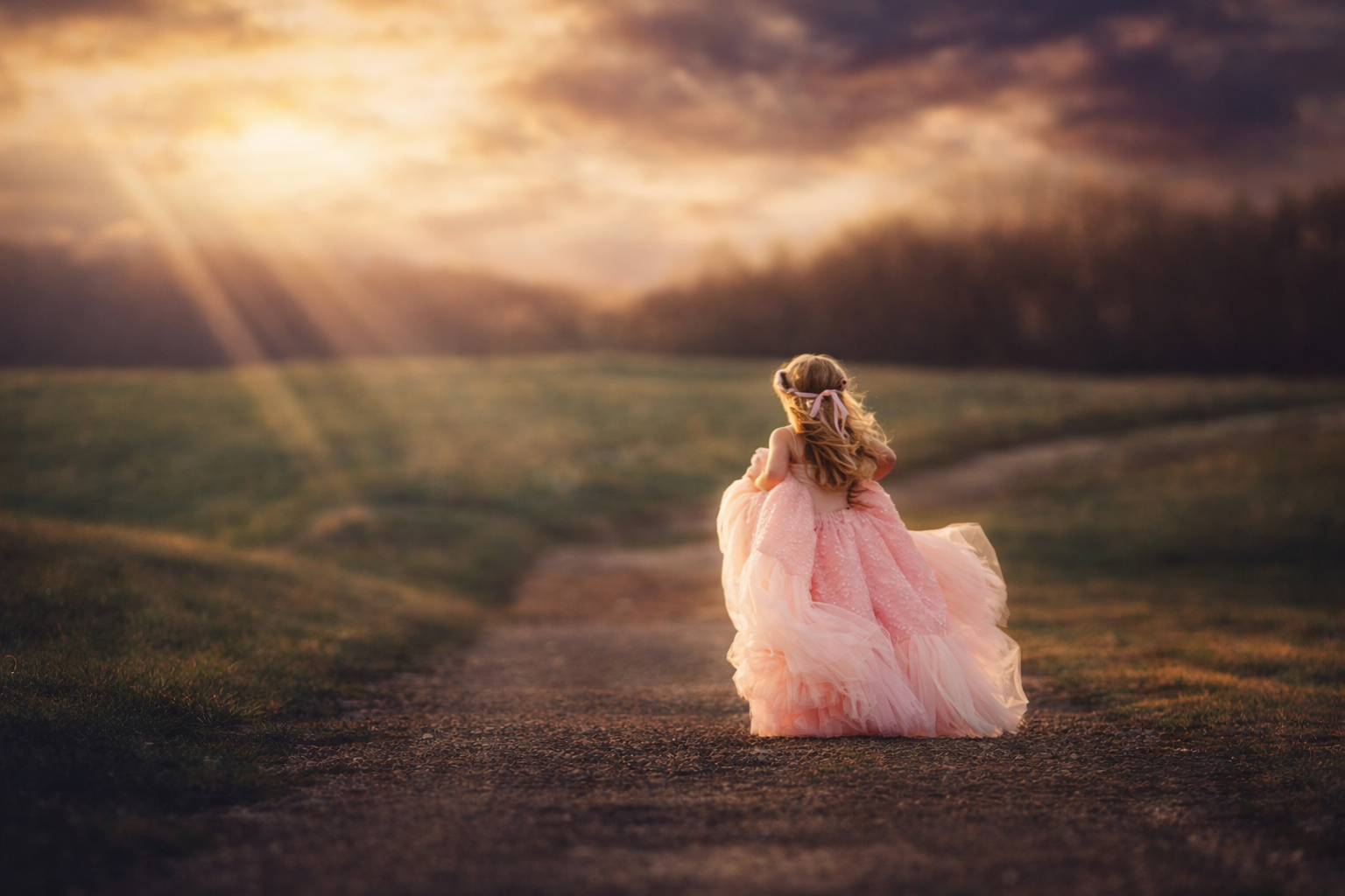 A young girl in a pink dress stands in soft sunset light, creating a timeless fine art children’s portrait with gentle movement and a warm, natural glow.