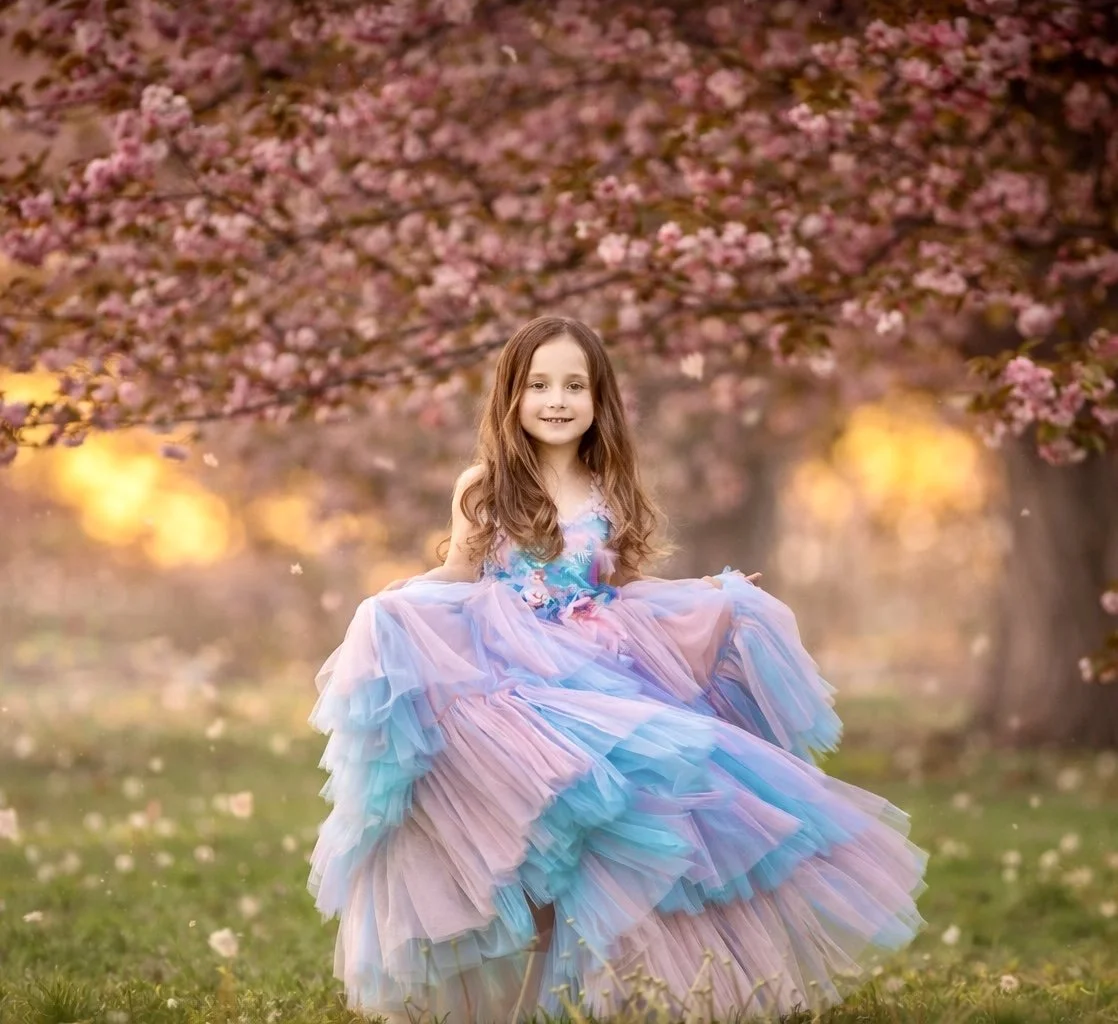 Young girl twirling in a blue dress beneath blooming cherry blossoms in Cherry Hill, New Jersey.