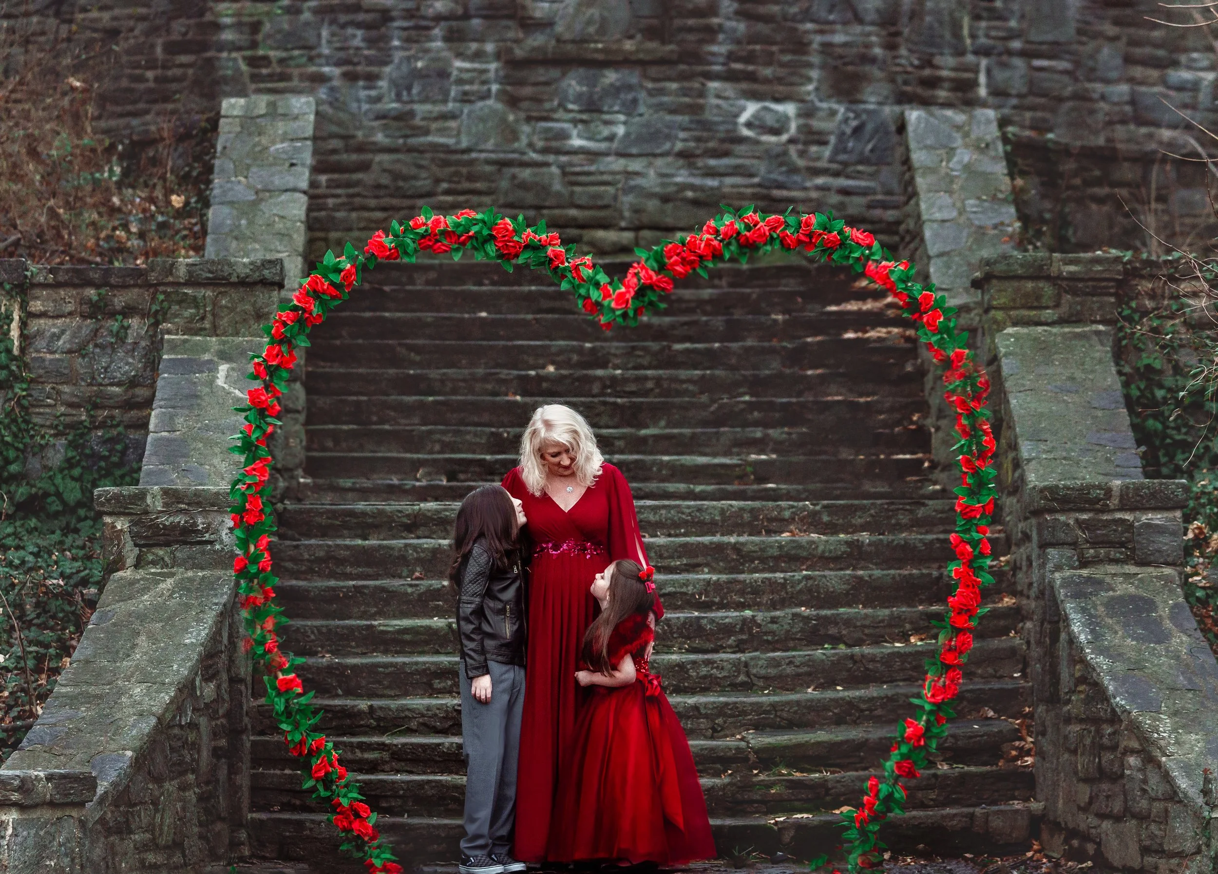 A fine-art Valentine’s portrait featuring a mother with her two children framed by a romantic floral heart arch, created for timeless family Valentine’s photography in New Jersey and Philadelphia.