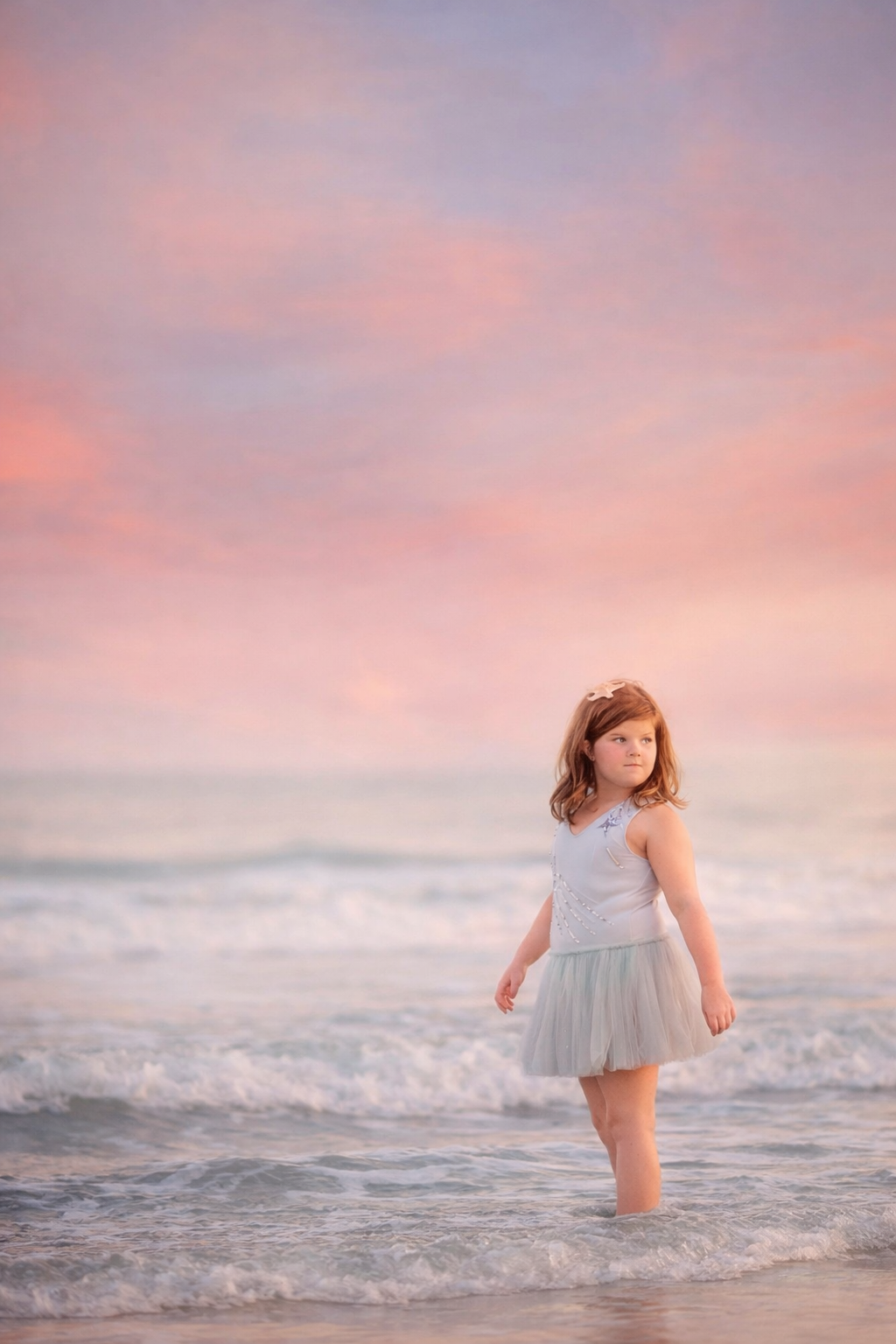 girl in a blue drss standing in the ocean during a Sea Isle City beach portrait session with soft pastel skies at sunset