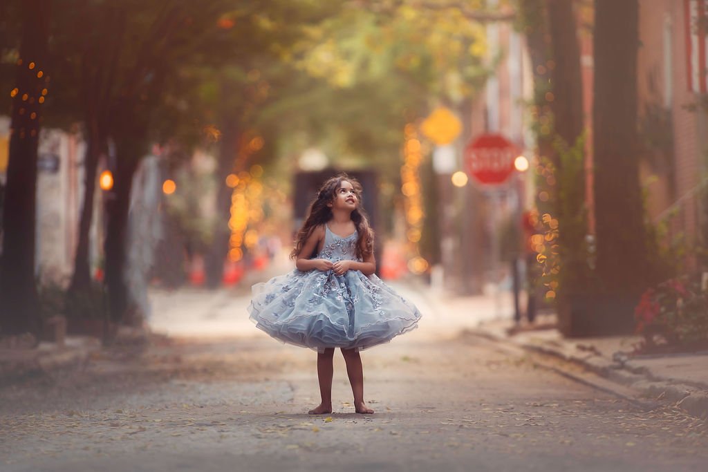 Little girl wearing a silver Anna Triant dress, smiling and looking up at the sky during a family session on Addison Street in Philadelphia.