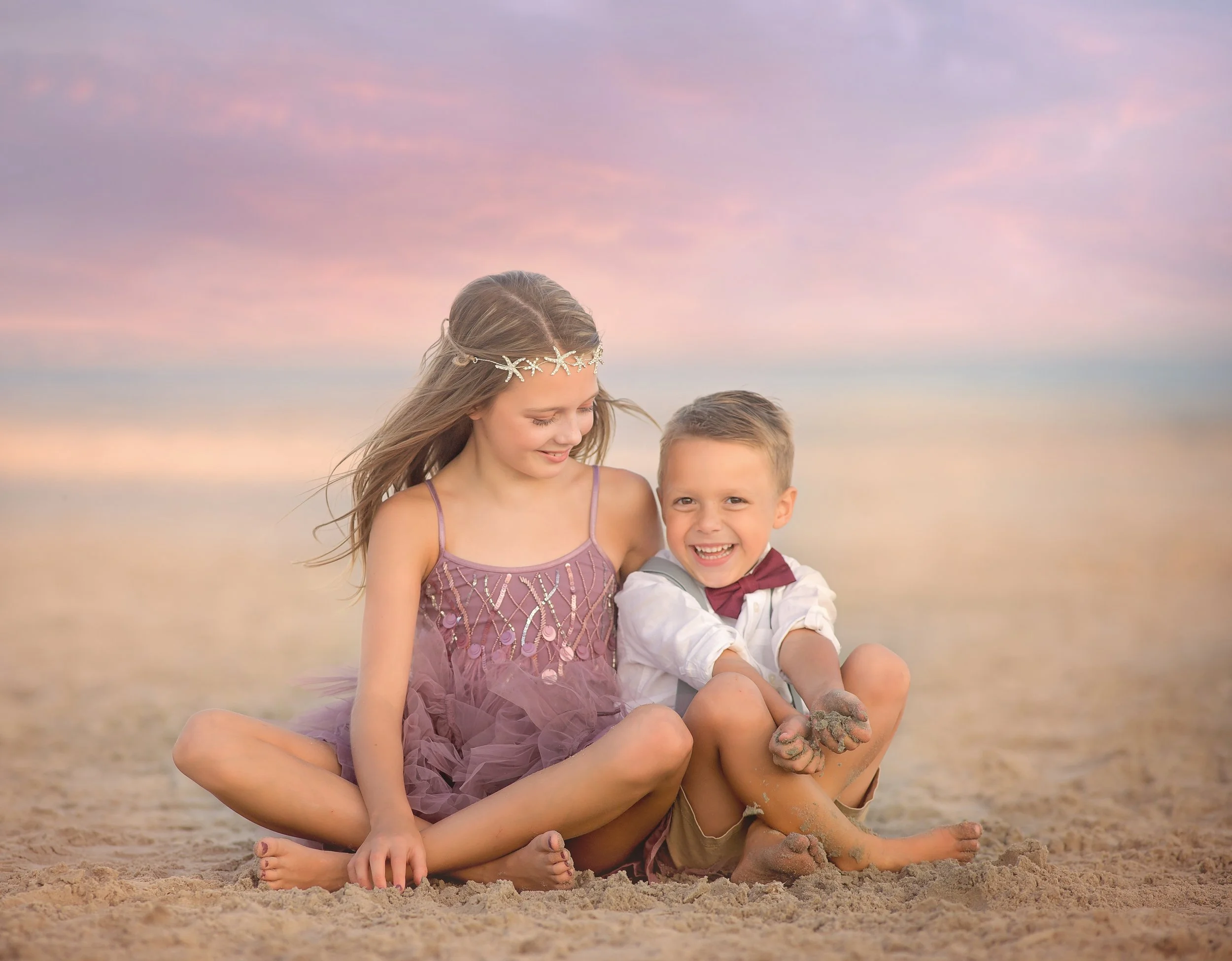 Brother and sister sitting on the beach laughing during a Wildwood NJ photography session captured by a South Jersey photographer.