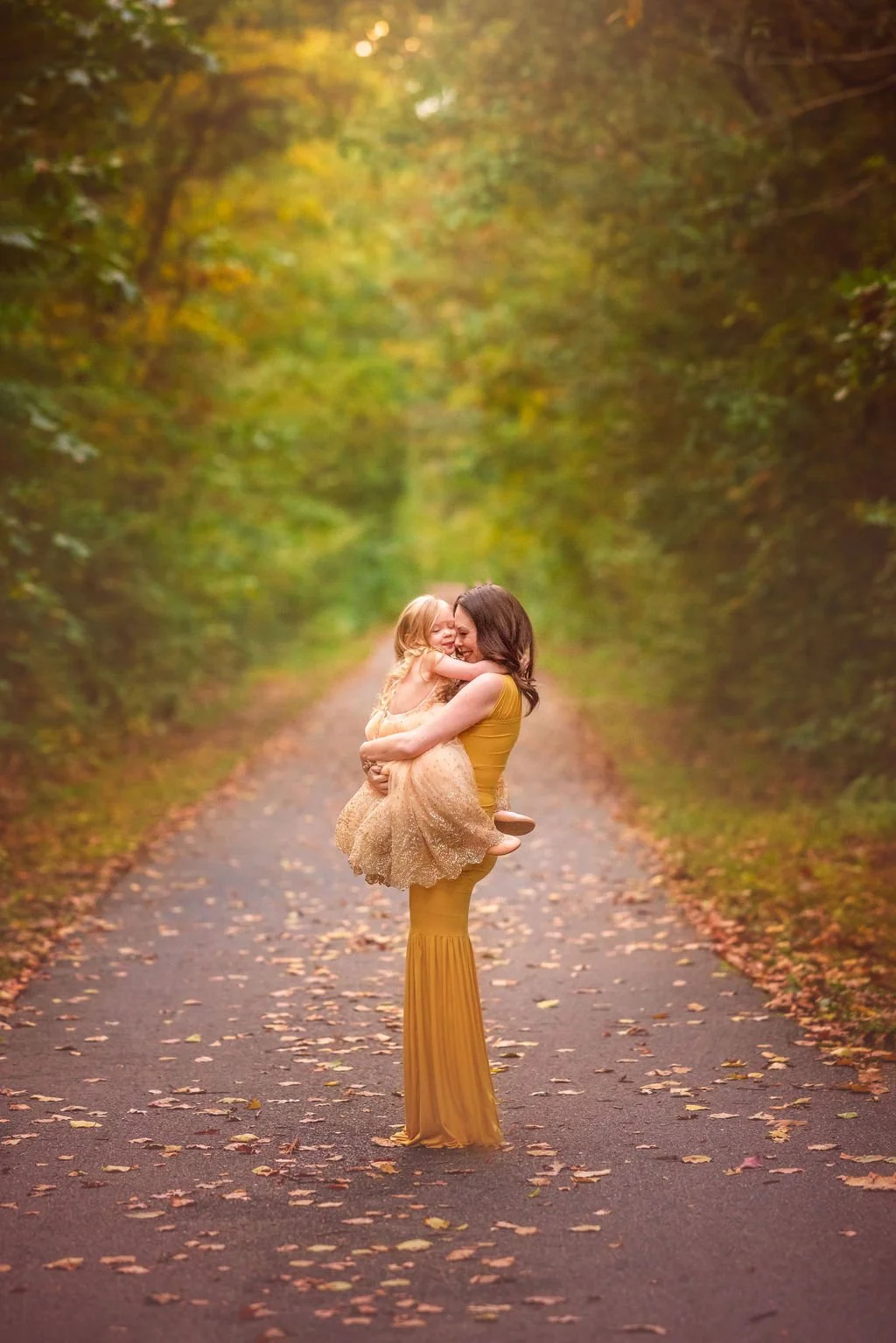Mother holding her young daughter over her pregnant belly while the child kisses her during an outdoor maternity session in South Jersey.
