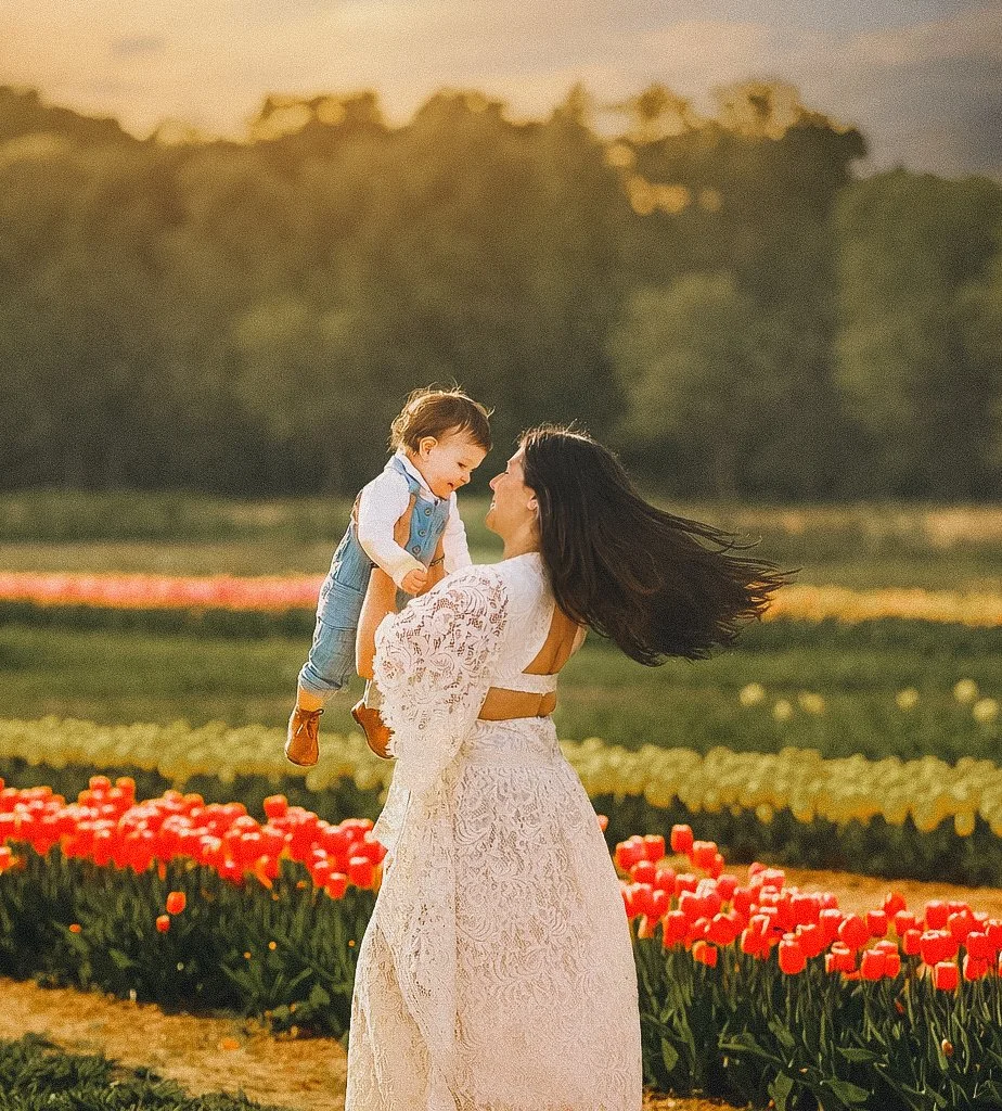 Mother holding her baby and smiling during a spring tulip photo session at Dalton Farms in South Jersey