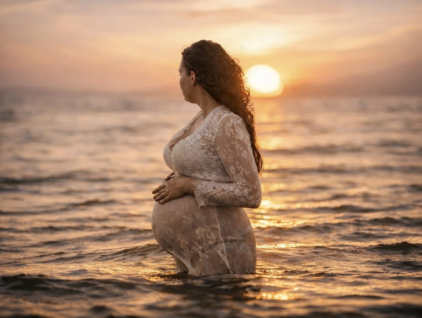 Expecting mother in flowing dress standing in the ocean at sunset during a Jersey Shore maternity photography session in New Jersey