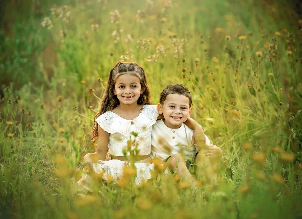 Children sitting and smiling in a wildflower field during a family maternity photography session in South Jersey.