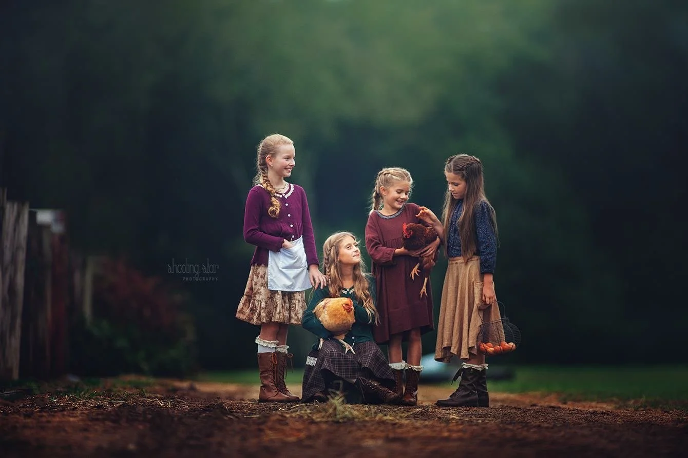 A small group of children pose together while holding chickens on a quiet farm, photographed in soft natural light for a fine art portrait that highlights connection, curiosity, and countryside charm in South Jersey.