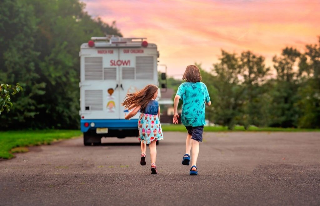 Siblings sharing a joyful moment while enjoying ice cream on a sunny day. and running towards mister softee
