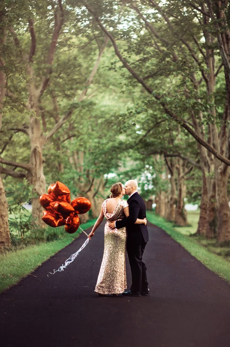 Fine art couples portrait of an engaged couple embracing on a tree-lined road during an elegant engagement session.