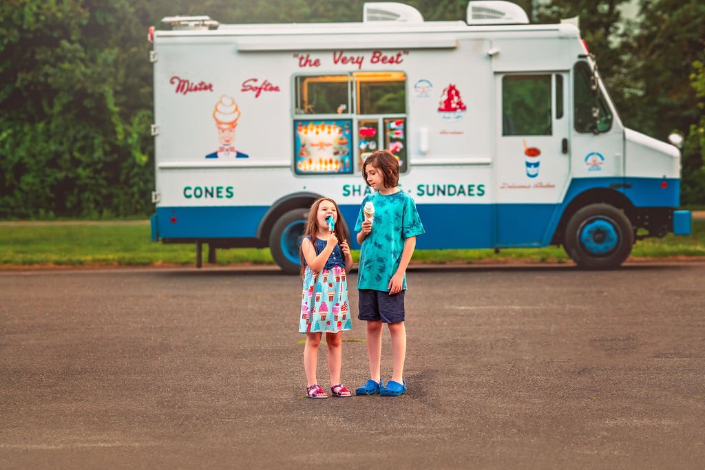 Playful siblings comparing their ice cream cones, laughing together.