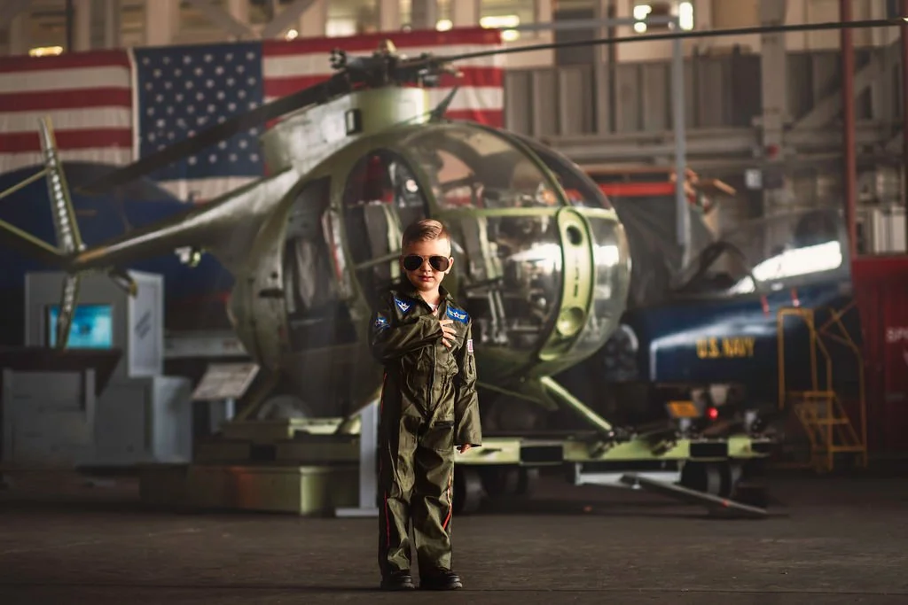 Boy wearing glasses with hand over heart standing in front of helicopter during aviation photoshoot near Cape May New Jersey