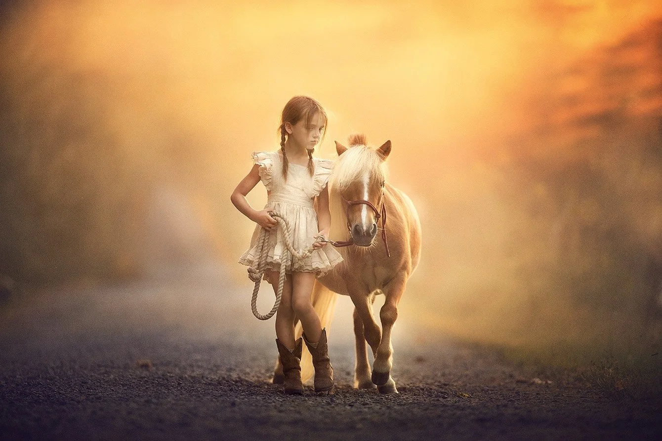 A young girl gently holds a pony in warm, glowing light, creating a timeless fine art portrait that reflects quiet connection, movement, and countryside beauty in South Jersey.