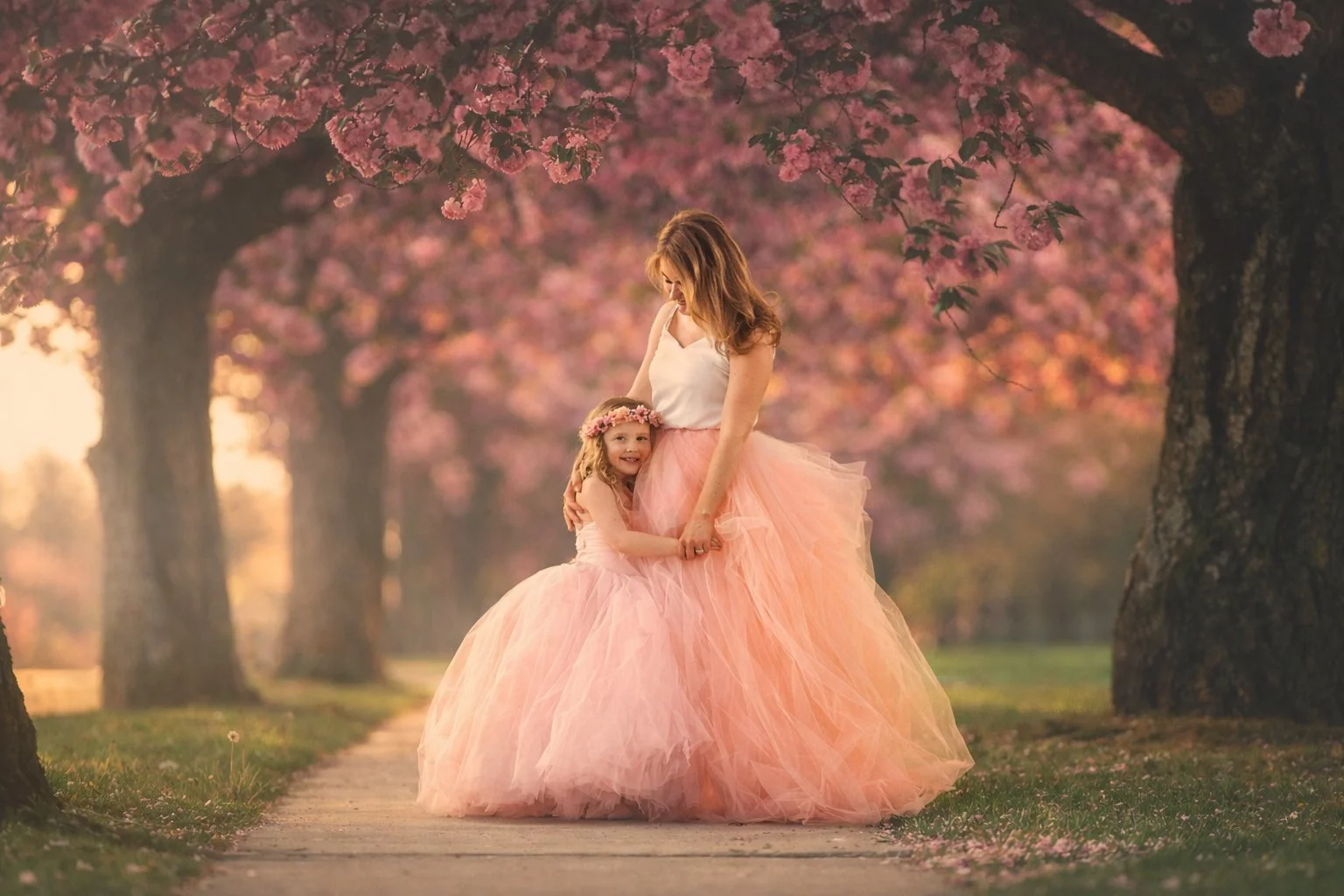 Little girl hugging her mother beneath blooming cherry blossom trees during a spring portrait session.