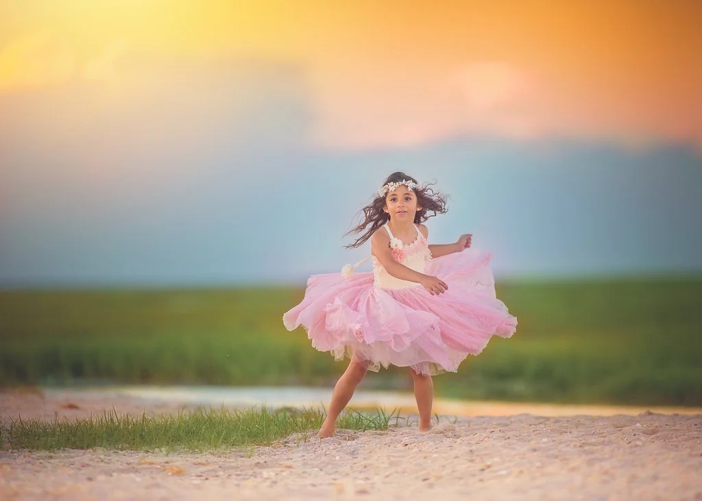 Golden hour birthday portrait of a little girl in a pink dress, twirling at the Jersey Shore with a pastel sky in the background, capturing the magic of her special day.