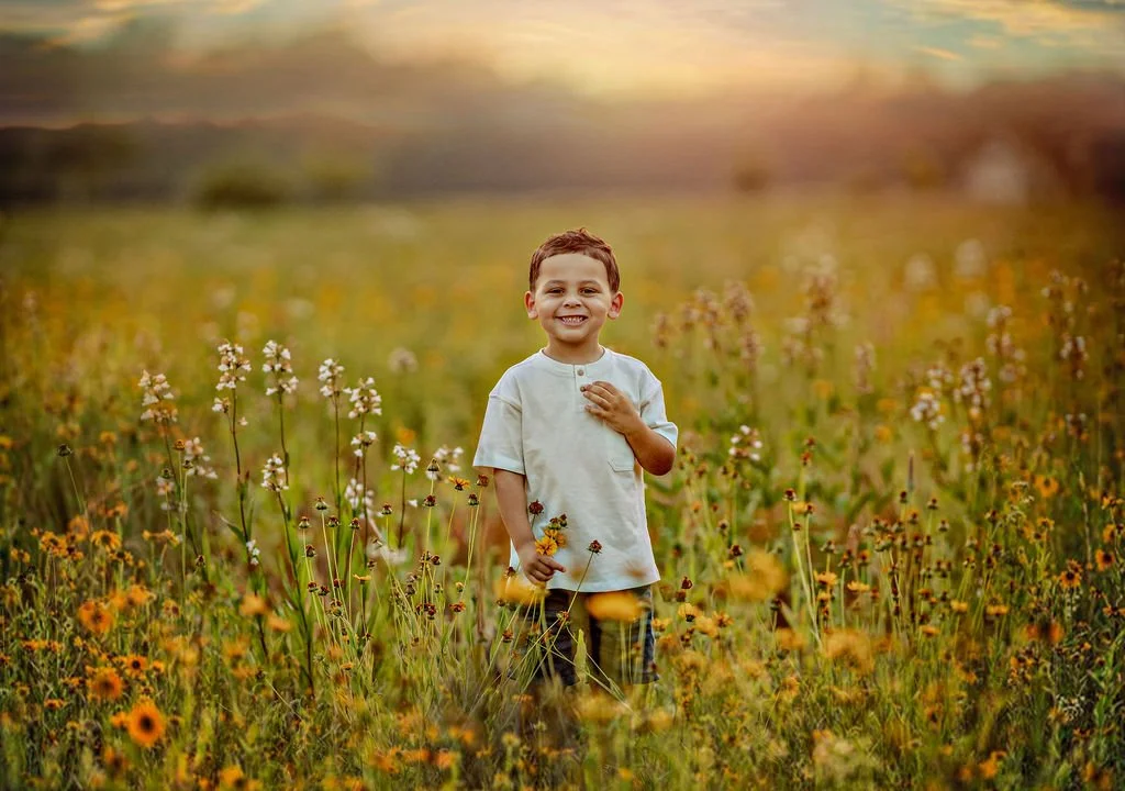 Young boy smiling in a wildflower field during a family maternity photography session in South Jersey.