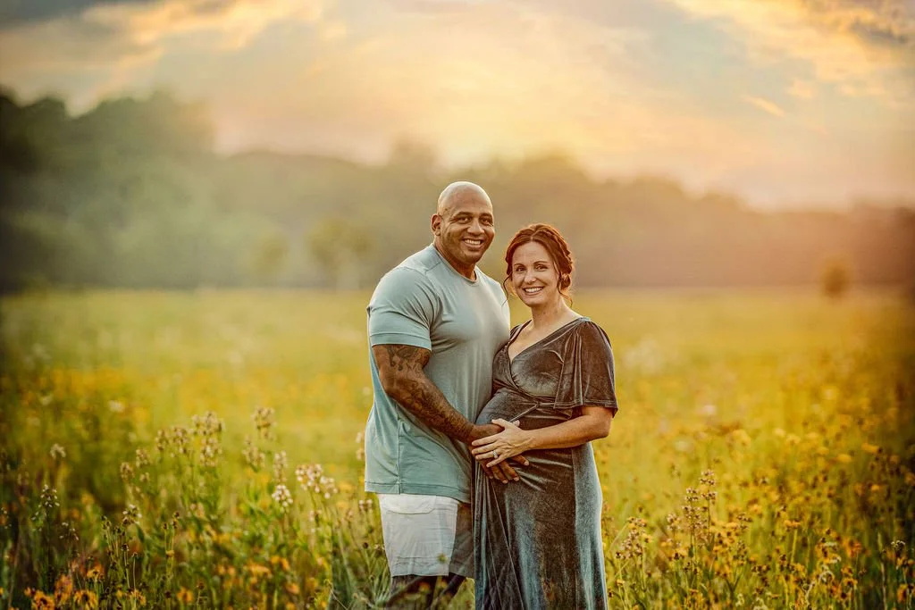 Father holding his pregnant partner’s belly during a maternity session in a wildflower field in South Jersey.