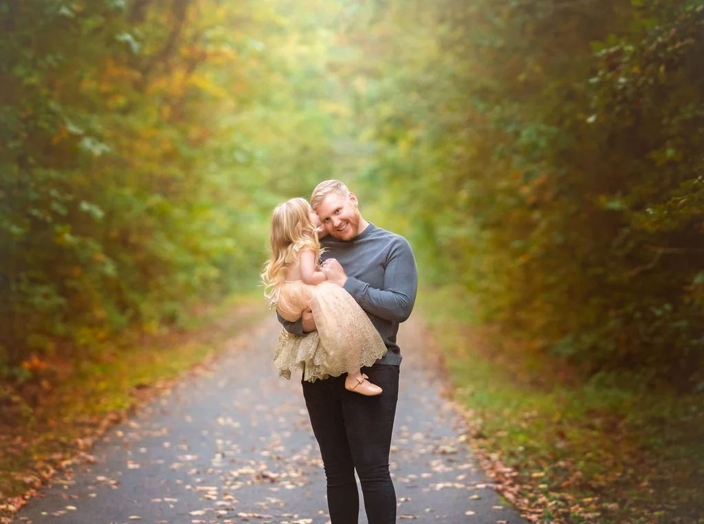 Father holding his young daughter while she kisses him during an outdoor family maternity photography session in South Jersey.