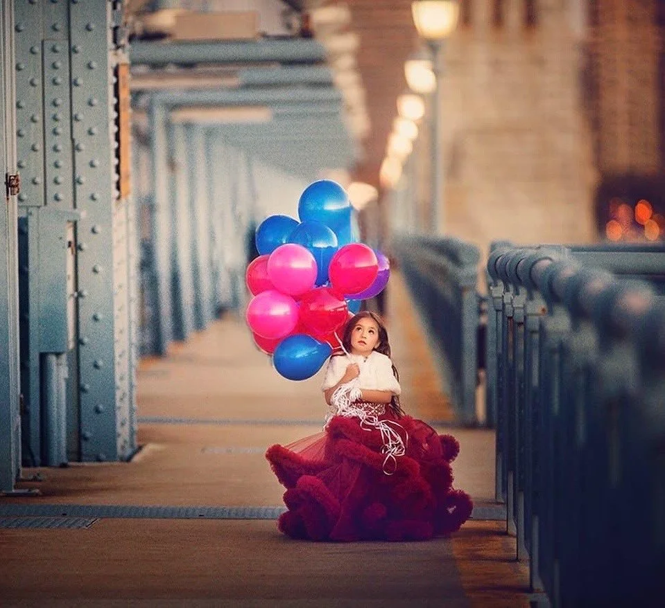 Young girl in a red dress holding balloons in a city setting during a family photography session