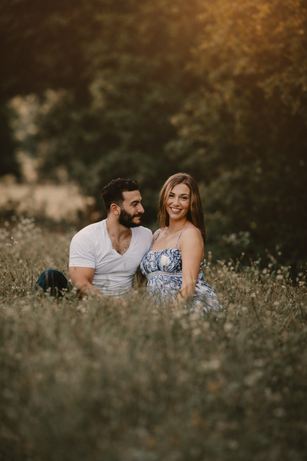 Expecting couple sitting together in a field during a fine art maternity photography session with soft natural light