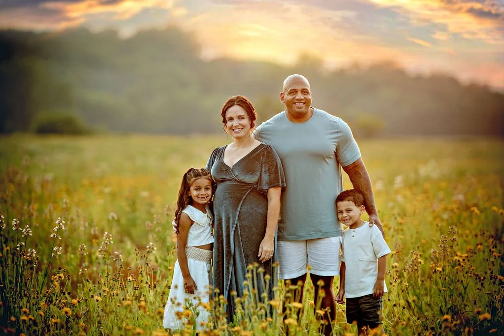 Family smiling together in a wildflower field during an outdoor maternity photography session in South Jersey.