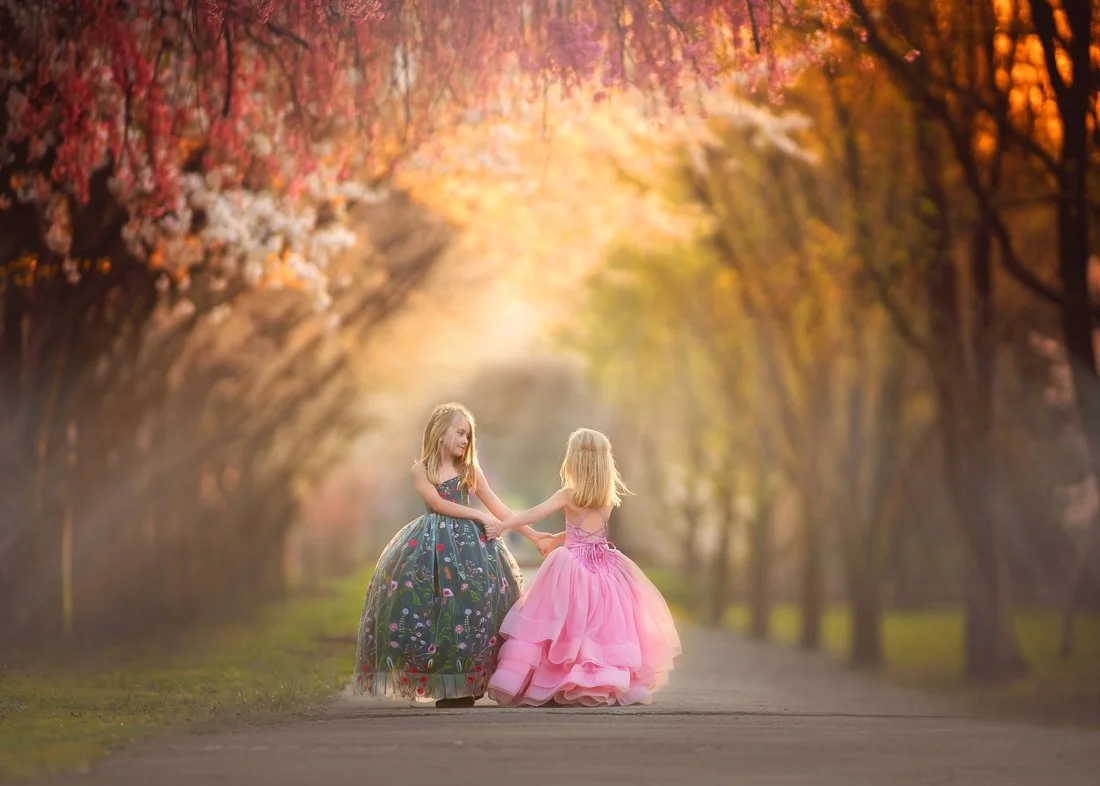 Joyful moment of sisters twirling in beautiful dresses among the greenery of Fairmount Park in Philadelphia.