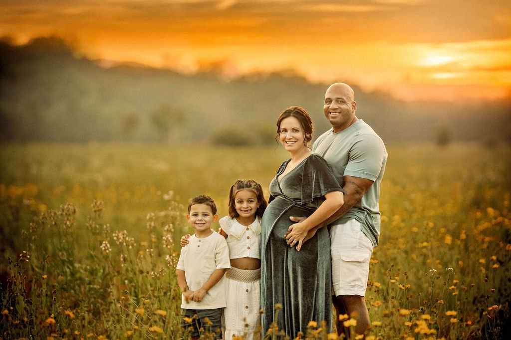 Family posing and smiling together in a wildflower field during an outdoor maternity photography session in South Jersey.