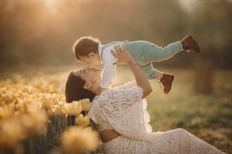 Mother lifting her young child into the air and kissing him during a golden hour fine art portrait session in South Jersey