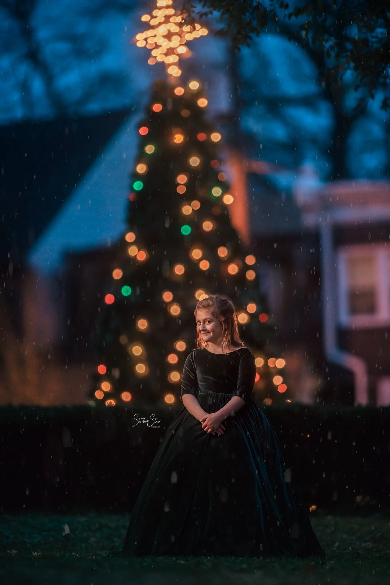 Little girl in dark dress standing in front of a glowing Christmas tree in Pitman NJ with falling snow