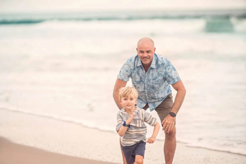 Little boy running away from his dad while playing on the beach during a family session in Atlantic City NJ.