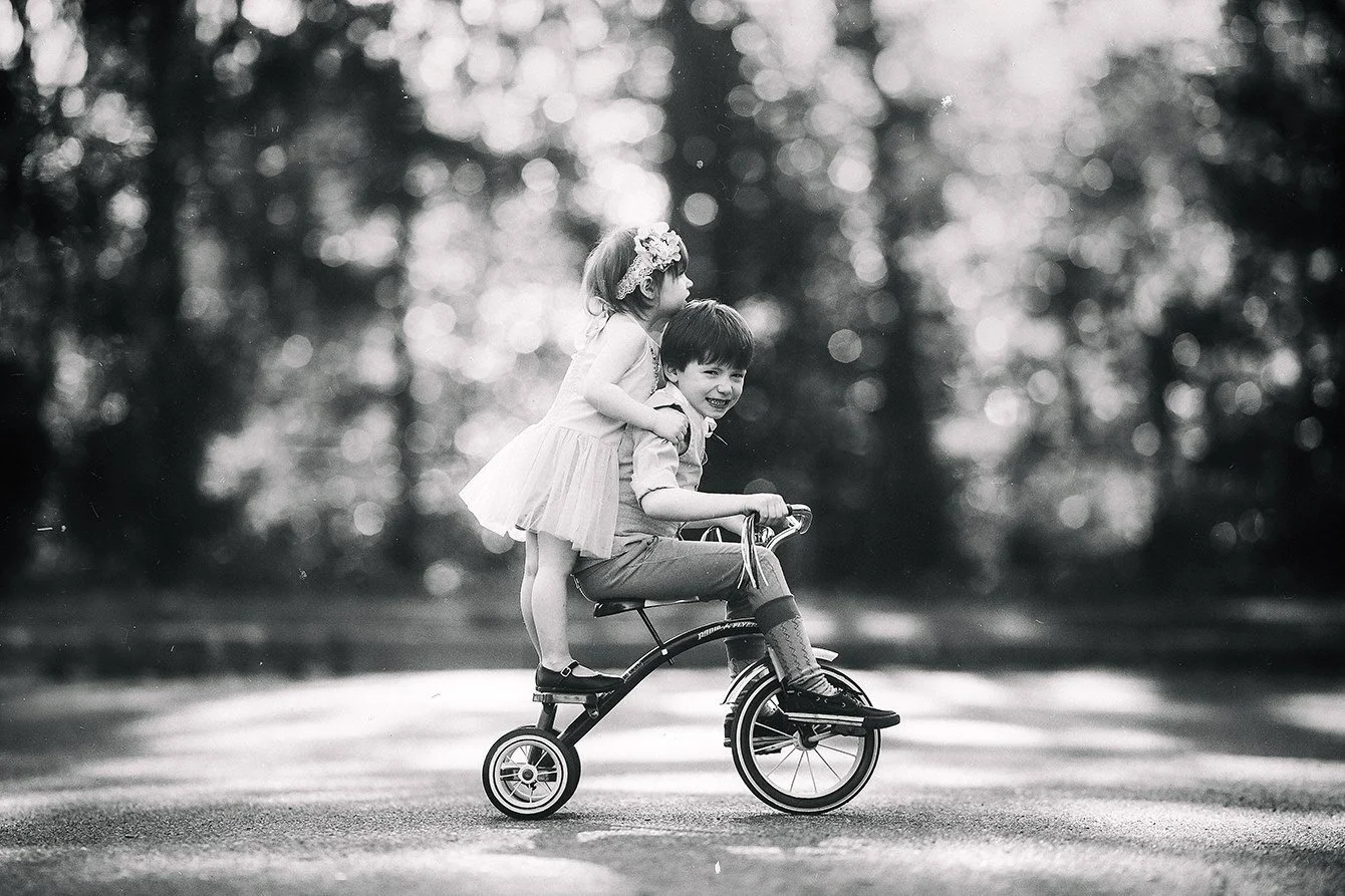 Rocco and Gigi riding a tricycle together during a black and white sibling portrait session at sunset in Woodstown, New Jersey.