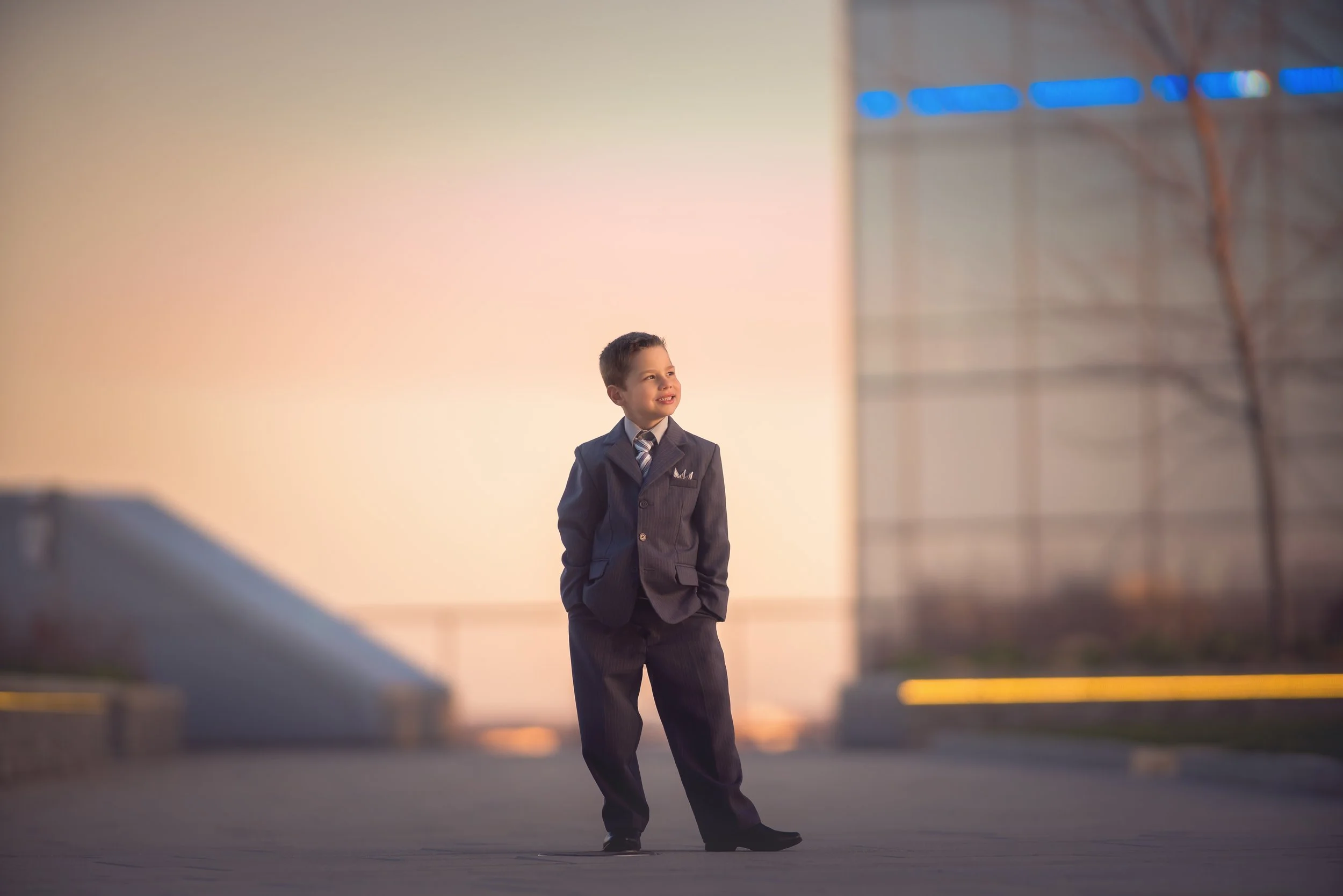 Young child in a suit photographed at Cira Green with the Philadelphia skyline in the background during a fine art family photoshoot.