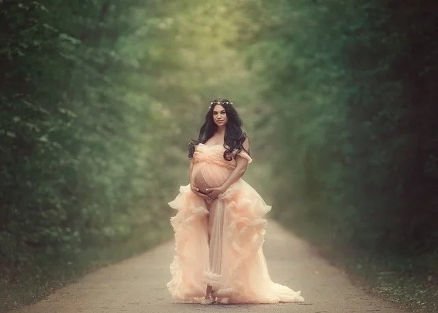 A serene fine-art-maternity-portrait of an expecting mother standing along a quiet forest path, wrapped in flowing peach couture. Soft light and gentle movement create a timeless, peaceful scene that honors the beauty and stillness of pregnancy. 