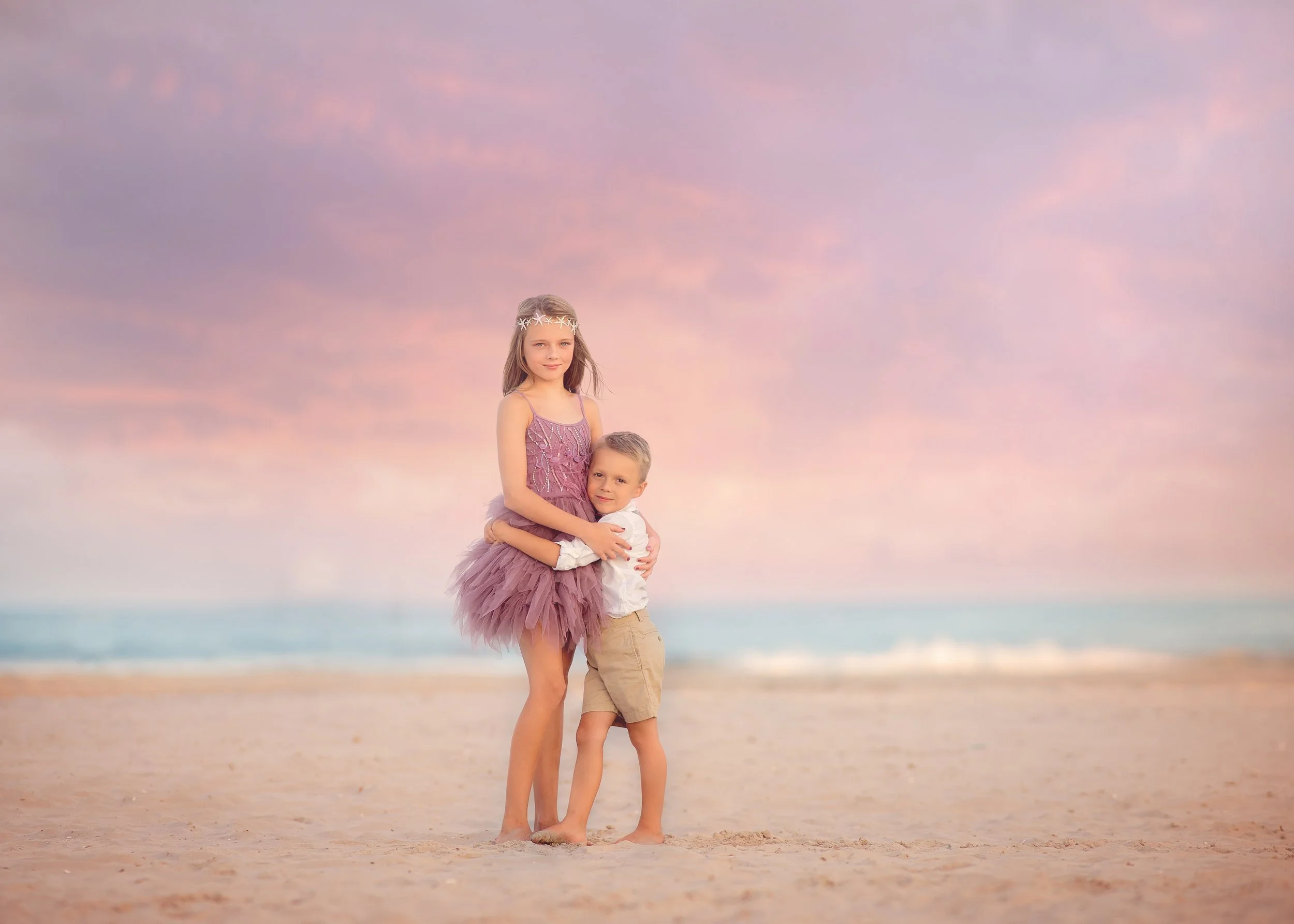 Brother and sister posing on the beach with ocean waves behind them during a portrait session in Wildwood New Jersey photographed by a Jersey Shore family photographer.