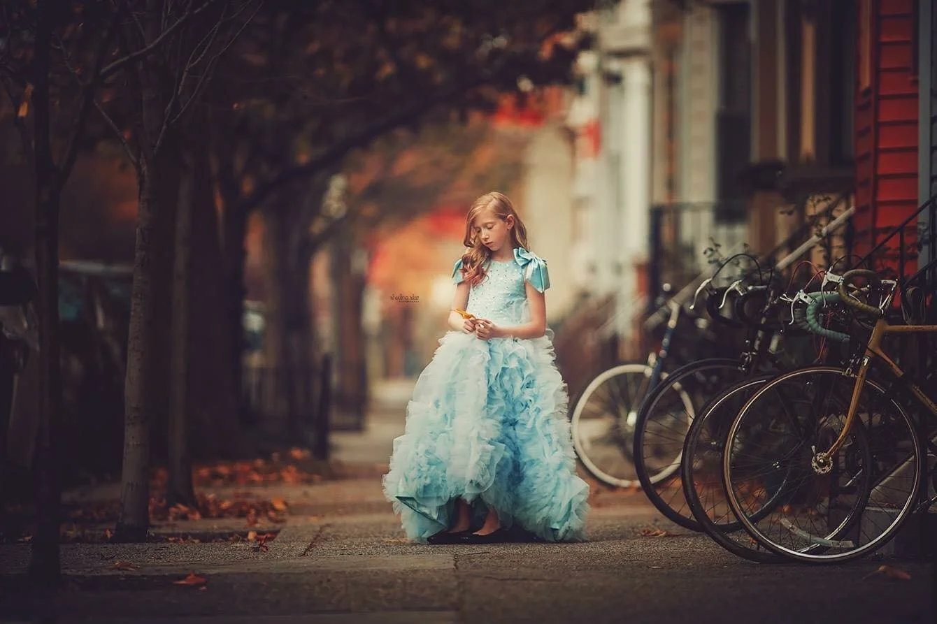 A striking fine art portrait of a young girl in a flowing blue dress, photographed in the heart of South Philadelphia. Clean lines, urban texture, and soft directional light come together for an editorial-inspired portrait that feels modern yet timel