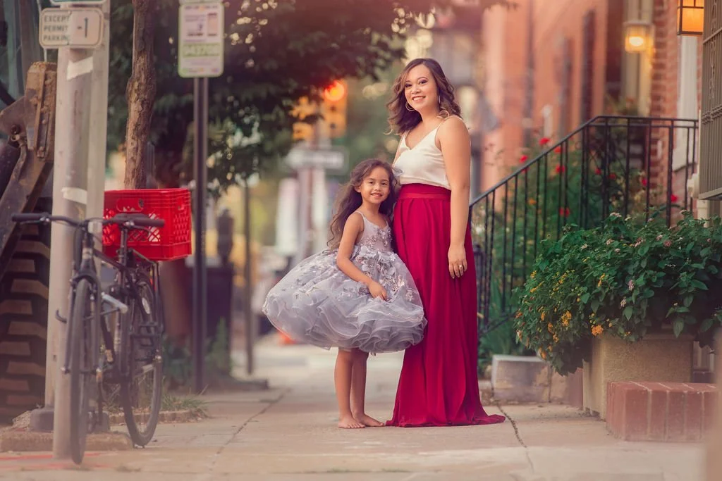 Mother posing with her older daughter wearing a silver dress on a city sidewalk during a family session in Philadelphia.