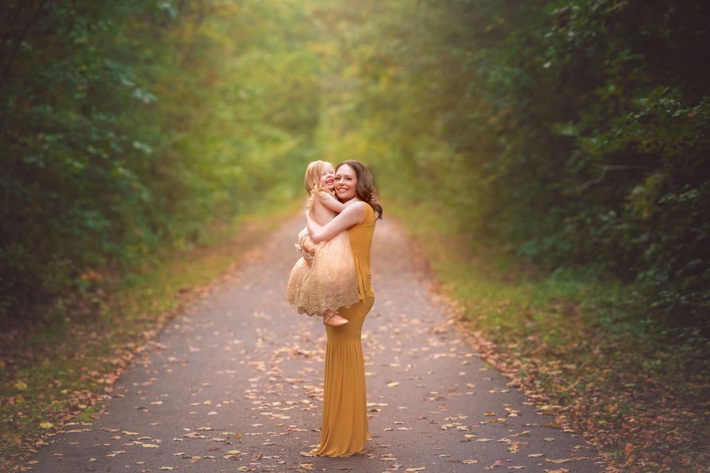 Pregnant mother holding her young daughter while they laugh together during an outdoor maternity photography session in South Jersey.