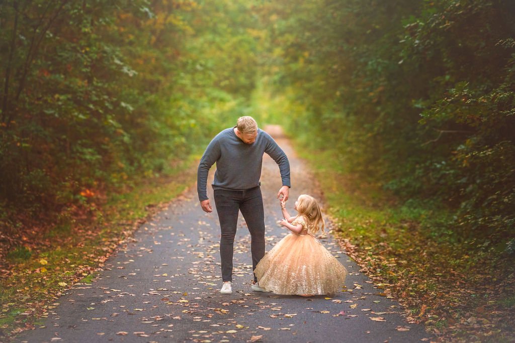 Father twirling his young daughter in the air during a joyful outdoor family maternity photography session in South Jersey.