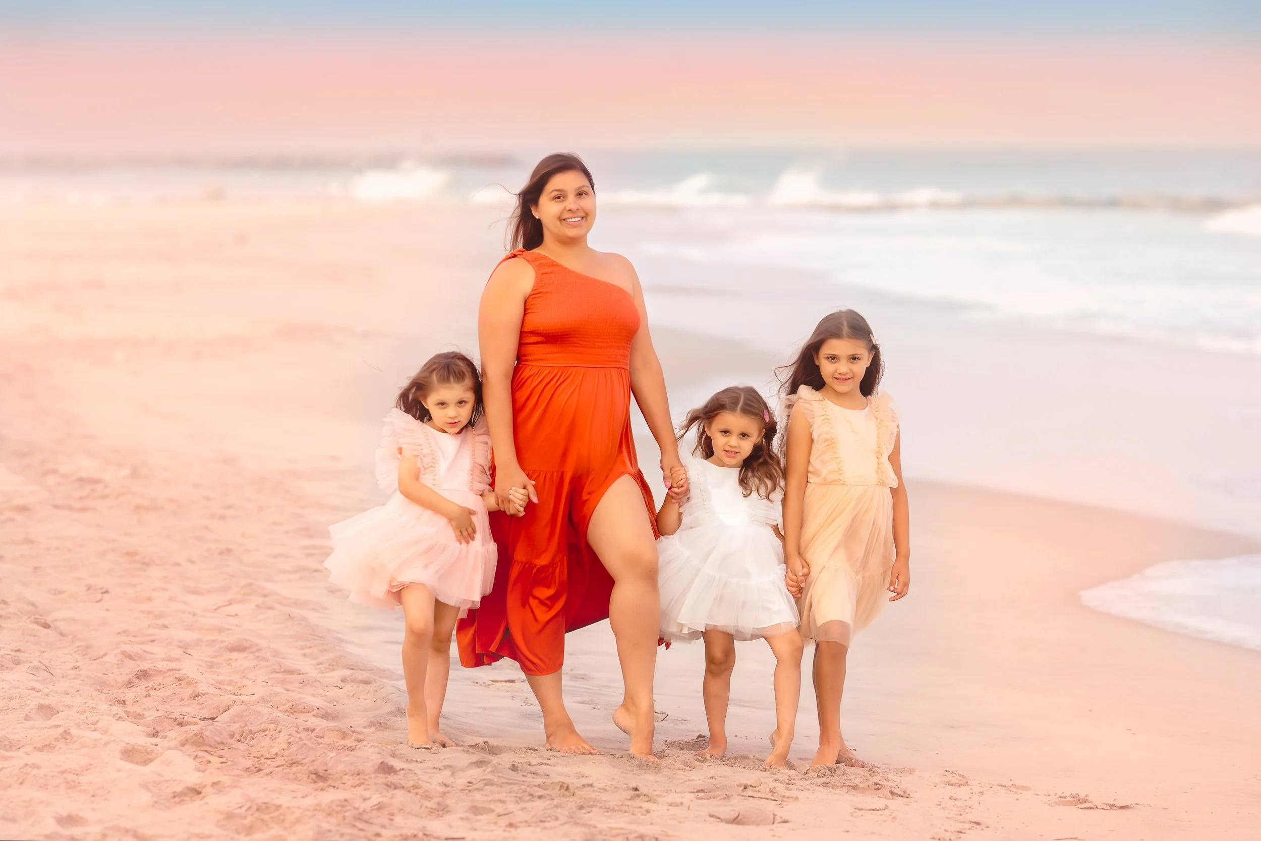 Mother in a red dress posing with her three daughters during a Cape May family portrait session