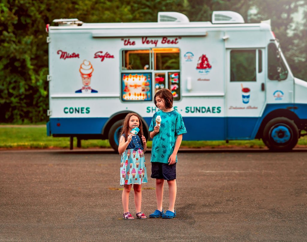 Brother and sister smiling with ice cream cones in hand, standing by the brightly colored Mister Softee truck